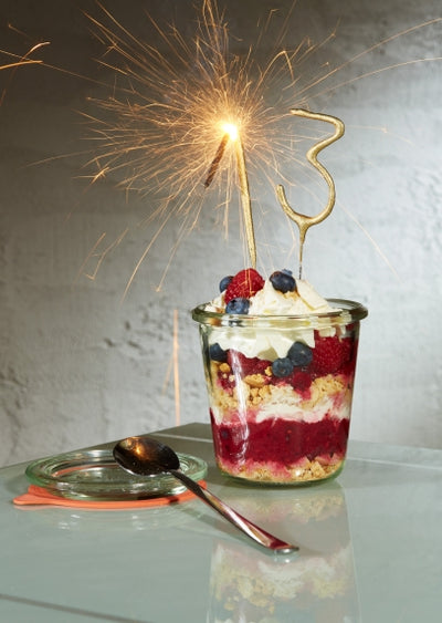 Tända sifferbloss i guld nedstucket i dessert med bär och grädde