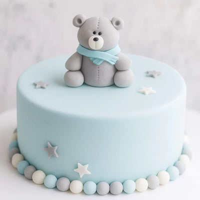 En ätbar nallebjörn i sockerpasta som dekorerar en blå tårta till baby shower