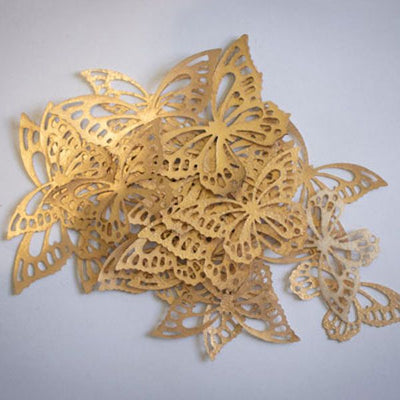 Ätbara fjärilar i guld, gjorda i wafer-paper. Fjärilarna ligger i en hög i mitten med vit bakgrund.