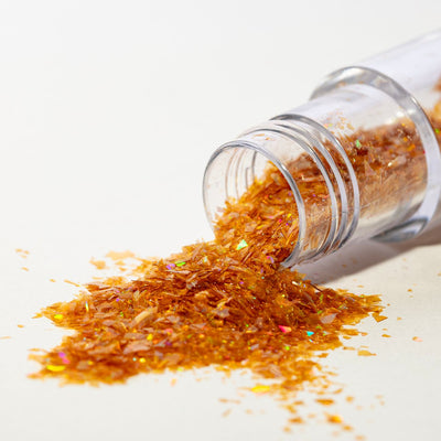 Öppen burk med PME Magic Sparkles i guld, glitterflingorna rinner ut mot vit bakgrund.