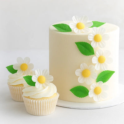 Vit tårta dekorerad med vita waferblommor och gröna blad från Wilton, somrig och elegant presentation.