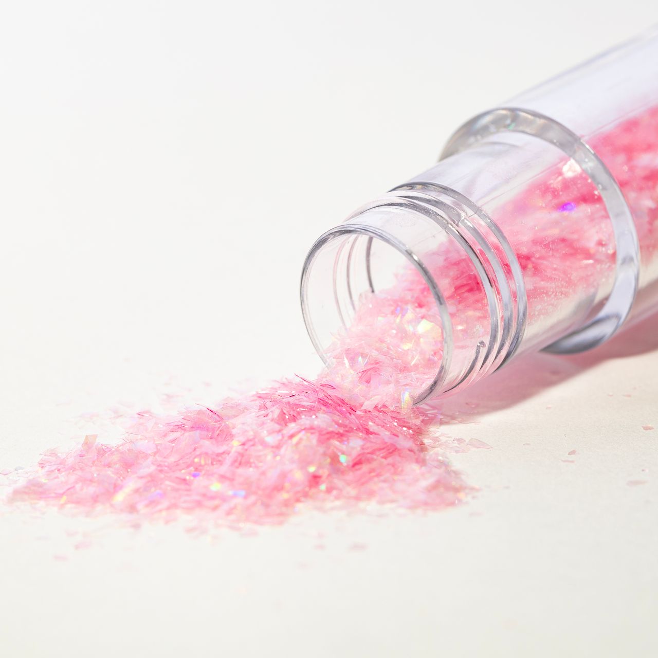 Öppen burk med rosa ätbara glitterflakes från PME som rinner ut på vit yta