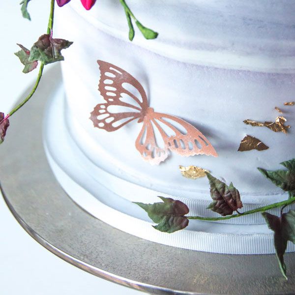 Ätbara fjärilar i roséguld som dekoration på en vit tårta