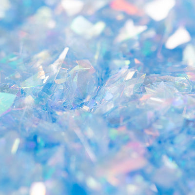 Närbild på skimrande, blå iriserande ätbara glitterflakes med ljusreflektioner.