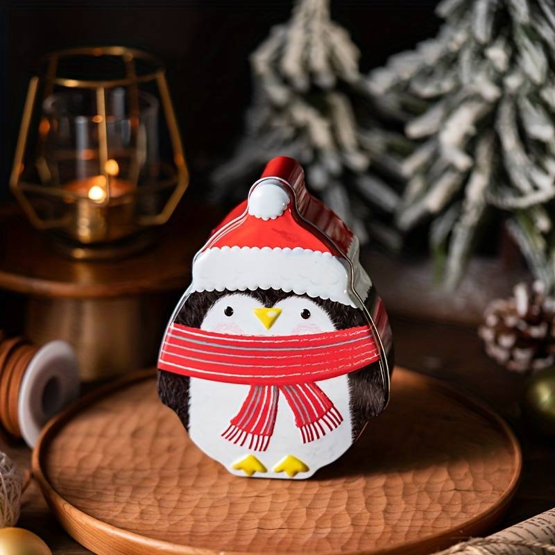 Plåtburk formad som en pingvin med tomteluva och röd halsduk placerad på ett trähfat i julmiljö
