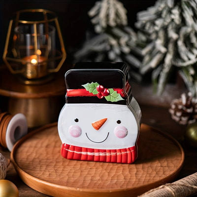 Plåtburk formad som en snögubbe med hög hatt och röd halsduk placerad på ett träfat i julmiljö