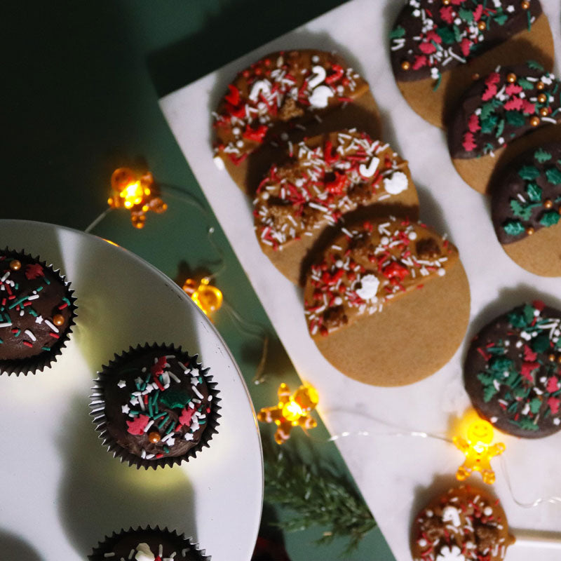 Juliga kakor och cupcakes dekorerade med färgglatt Happy Holiday-strössel på ett festligt dessertbord.
