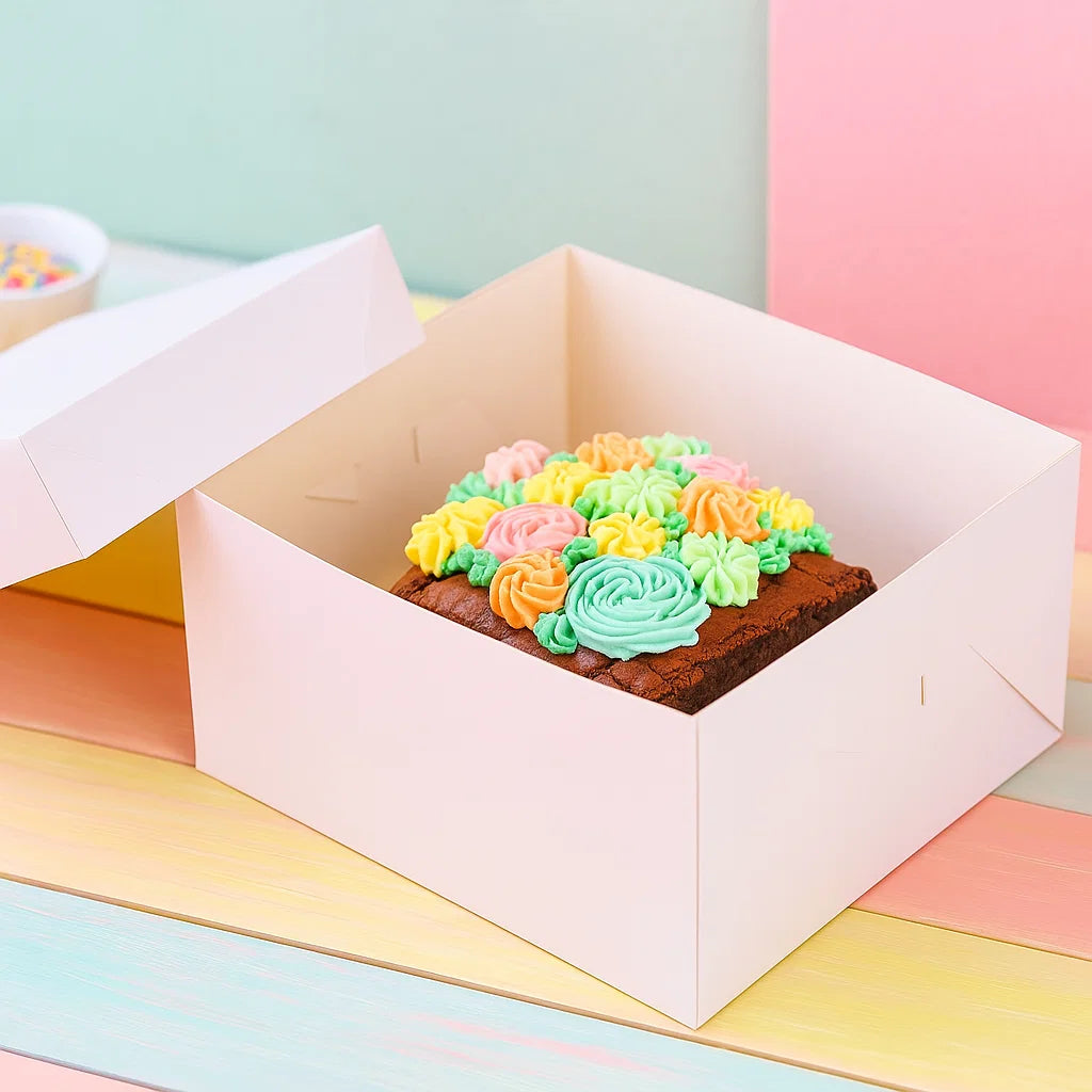 Vit tårtkartong från Funcakes, med locket vid sidan av. I tårtkartongen finns en brownie med spritsade blommor i pastellfärger. 