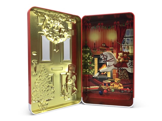 Öppen plåtburk med guldpräglad insida och julmotiv med brasa och leksaker