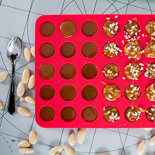 Röd silikonform fylld med knäck och knäck med hackad mandel.