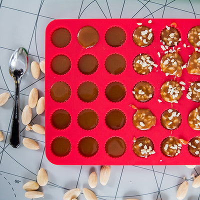 Röd silikonform fylld med knäck och knäck med hackad mandel.