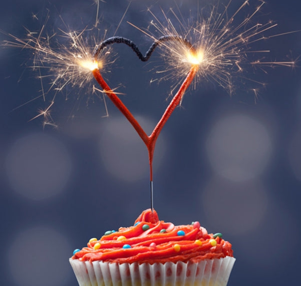 Brinnande hjärtformat tomtebloss placerat i en cupcake som gnistrar i mörk miljö.