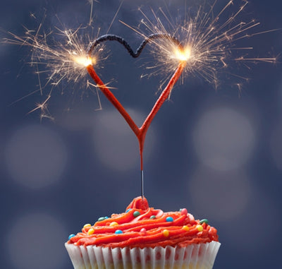 Brinnande hjärtformat tomtebloss placerat i en cupcake som gnistrar i mörk miljö.