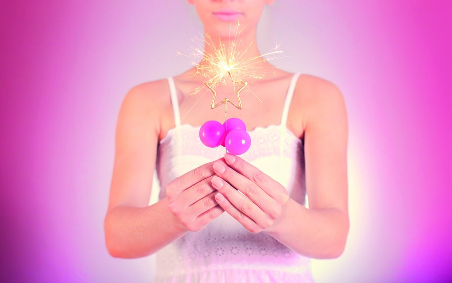 Person håller ett brinnande guldstjärna-tomtebloss i ljus rosa miljö.